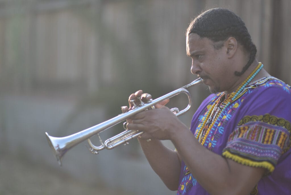 Josef Leimberg playing trumpet outdoors in a purple dashiki