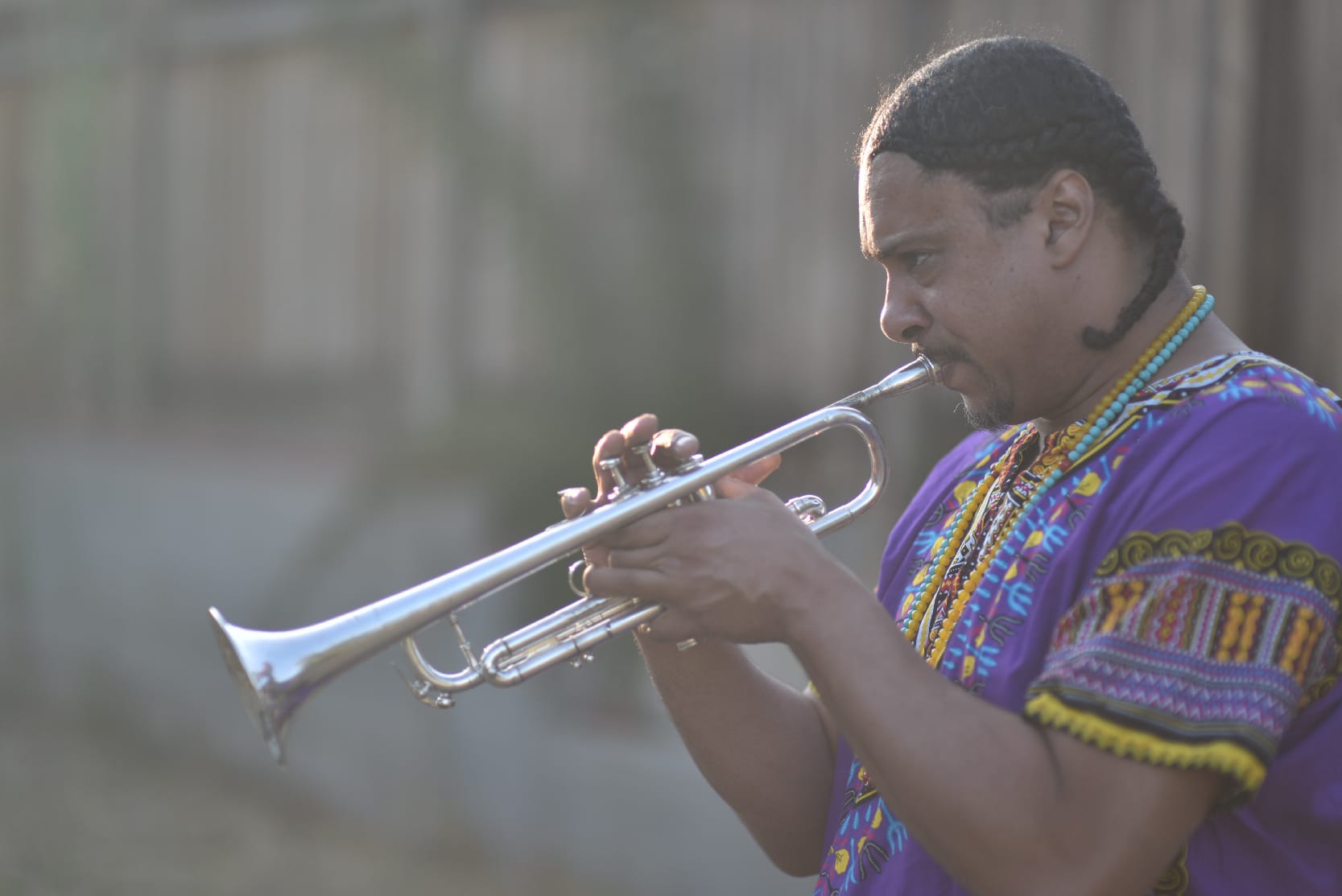 Josef Leimberg playing trumpet outdoors in a purple dashiki