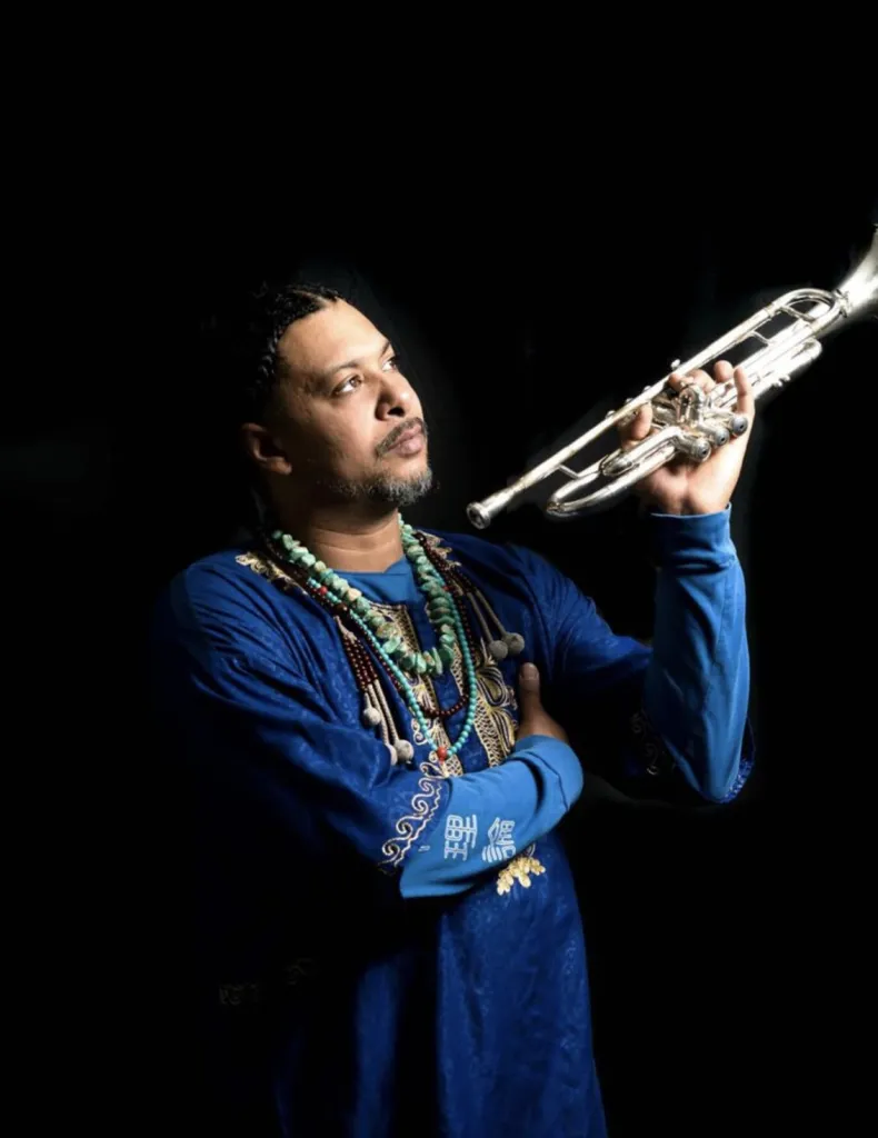Josef Leimberg holding his trumpet, wearing a blue embroidered tunic and turquoise beads